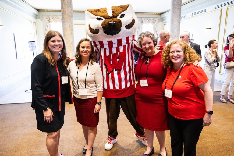 Four women flank Bucky Badger, smiling at the camera for a group photo.