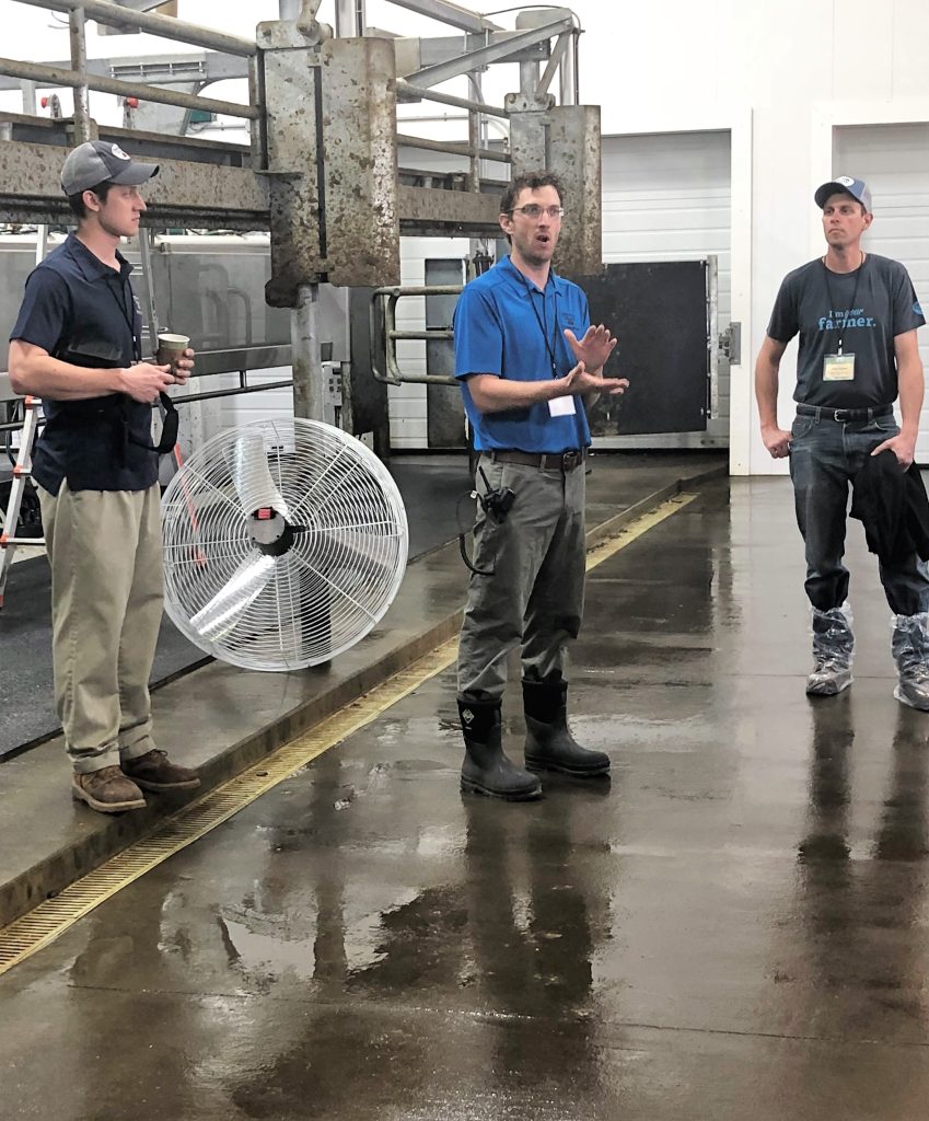 Three men standing in a building one man in a blue shirt is talking
