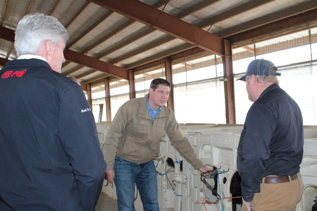 Three men standing in barn talking to one another holding equiptment
