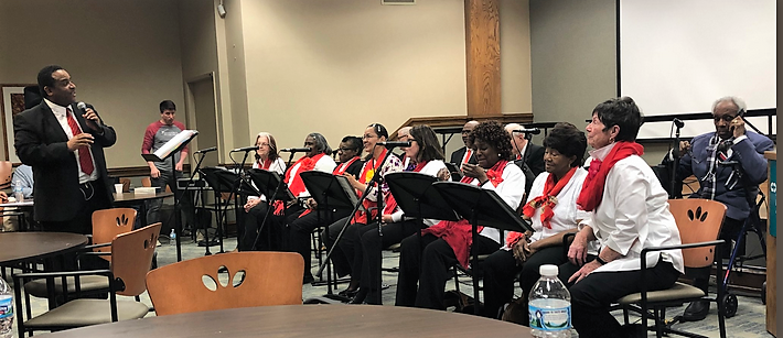 10 indivuduals with music stands positionind in front of them, one person stands apart conducting them