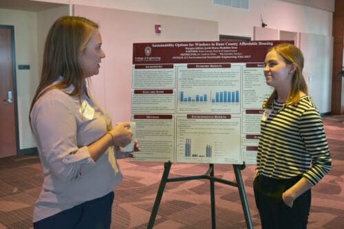 Two women facing each other talking with a posterboard behind them