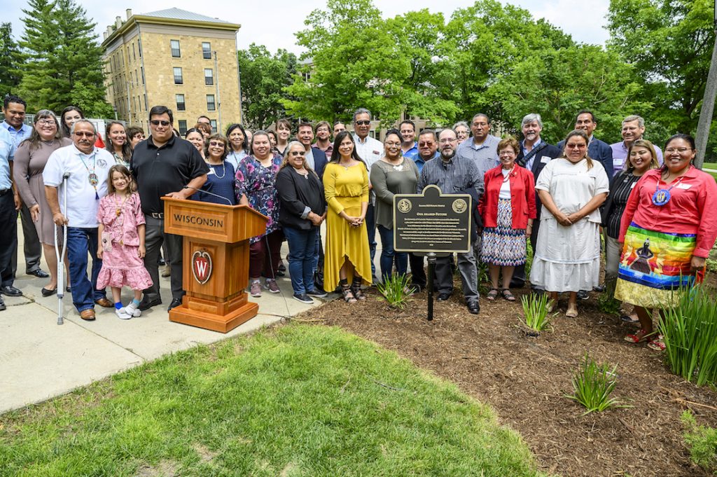 Group of people pose around a plaque