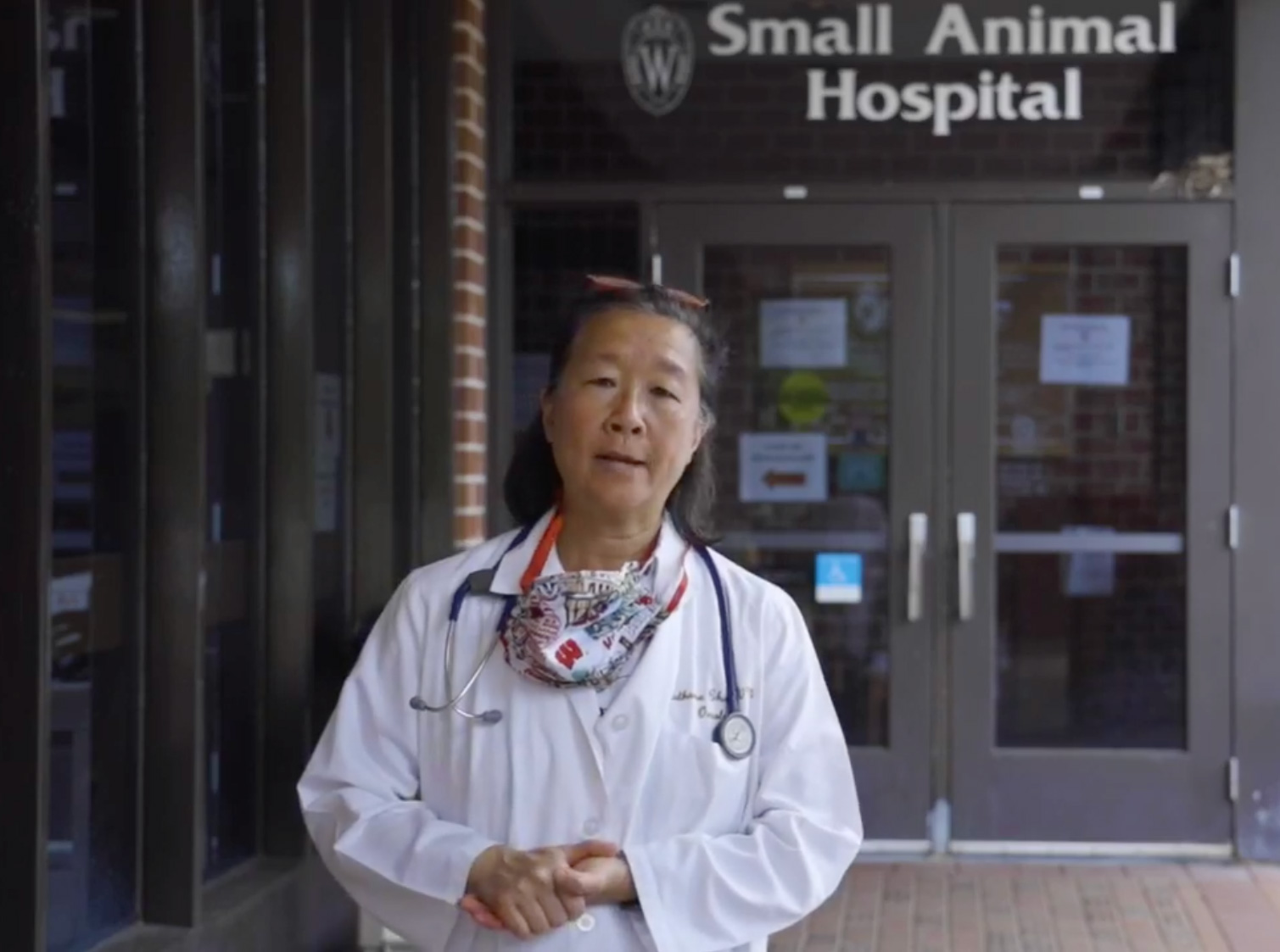 A female veterinarian in a white lab coat and stethoscope stands outside the entrance of the University of Wisconsin Small Animal Hospital.