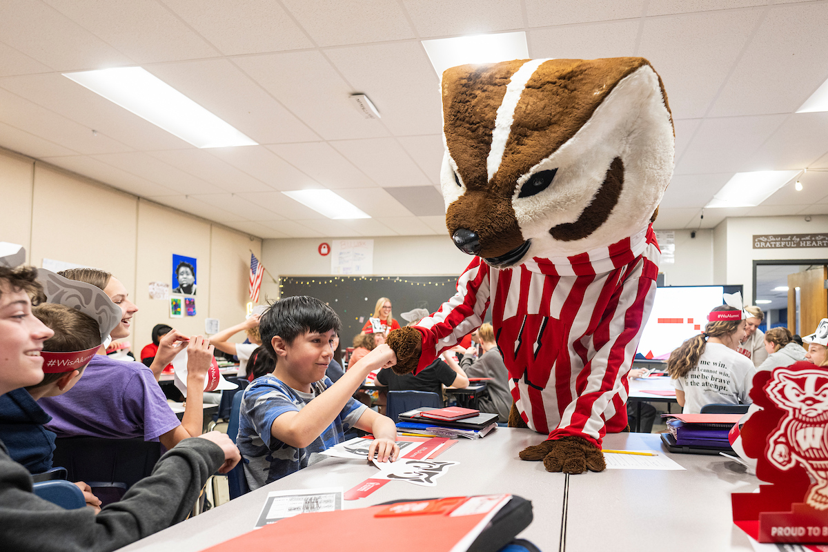 UW mascot Bucky Badger high-fives a K-8 student in a classroom.